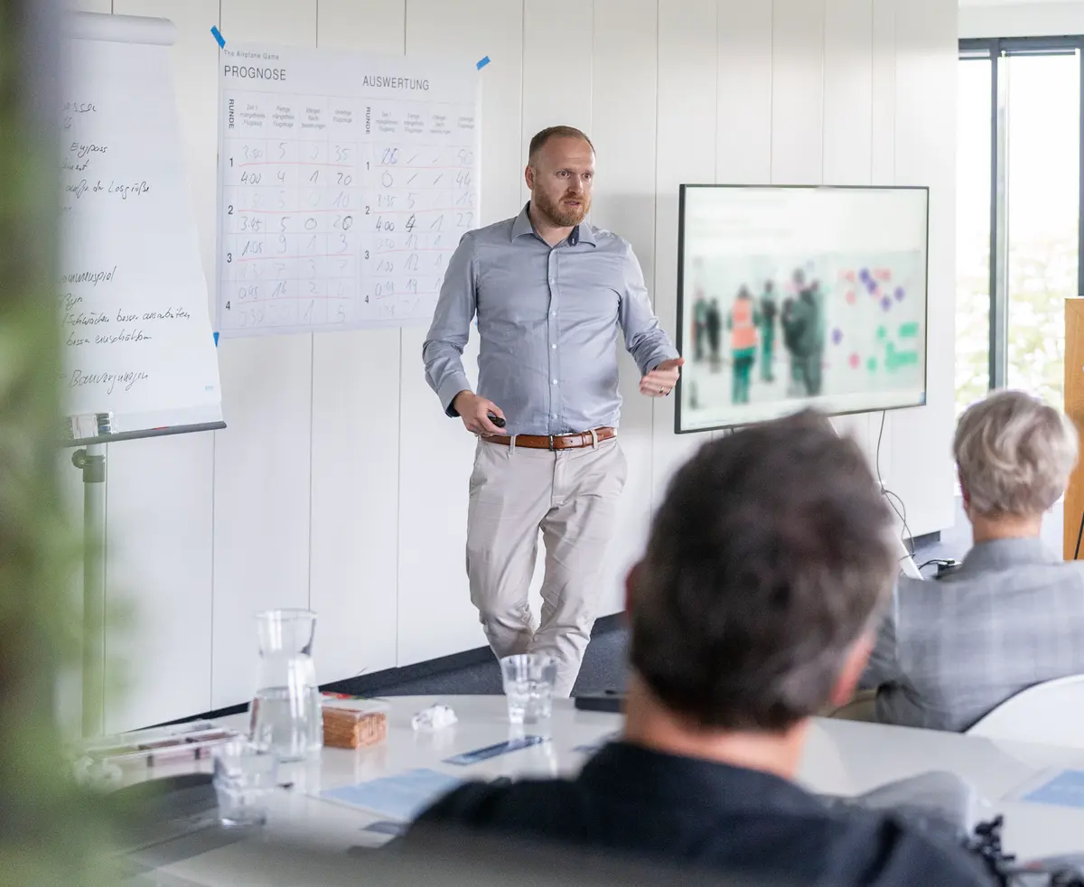 René Huppertz steht in einem Seminarraum neben Flipchart und Planungstafel und erklärt.